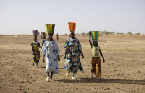 A group of women walking in the desert, carrying buckets of water on their heads.