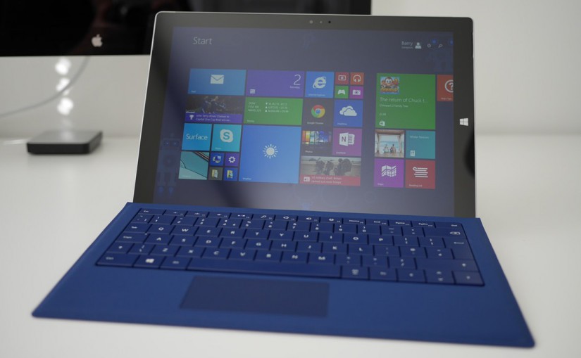 A Microsoft Surface Pro 3, with a blue keyboard, displaying the Windows 8 tiled start menu.